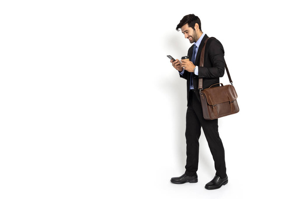Retrato de hombre de negocios feliz en traje escribiendo o usando teléfono móvil con bolsa de cuero marrón aislado sobre fondo blanco - Foto, Imagen