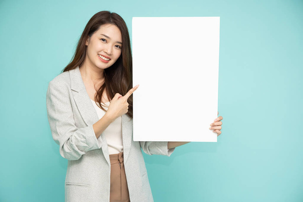 Mujer de negocios asiática señalando y sosteniendo cartelera blanca en blanco aislada sobre fondo verde - Foto, imagen