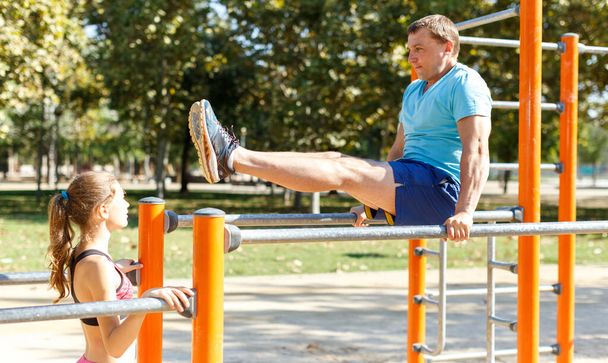 Man showing to daughter exercises on parallel bars - Foto, afbeelding