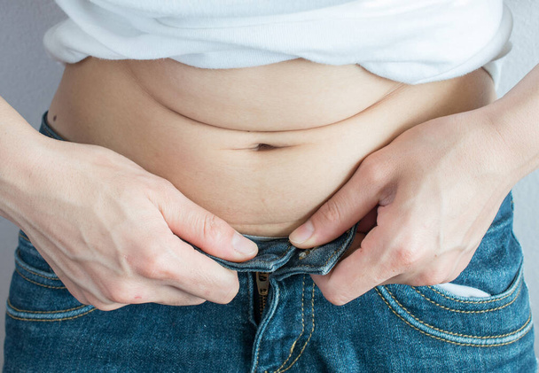 Close-up of fat woman with overweight waist trying to wear tight jeans but cannot button. Conceptual of overweight or diet background. - Foto, Imagem