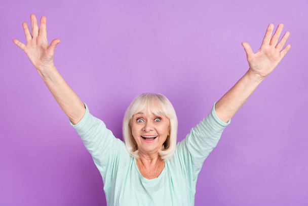Photo of excited funny crazy positive lady raise arms open mouth wear teal shirt isolated violet color background - 写真・画像