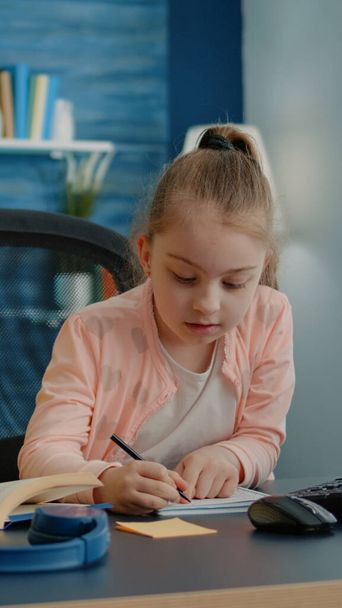 Petite fille écrit sur ordinateur portable avec stylo tandis que la mère donne de l'aide - Photo, image