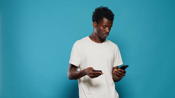 Genç adam akıllı telefondan online alışveriş için kredi kartı kullanıyor. - Fotoğraf, Görsel