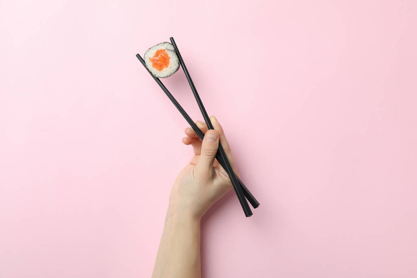 Female hand hold chopsticks with maki on pink background - Photo, Image