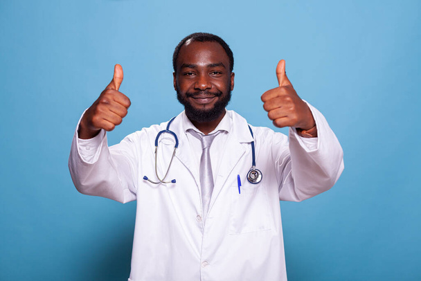 Afro-Amerikan doktorların, steteskopla tıp üniforması içinde baş parmak gösteren portresi. - Fotoğraf, Görsel