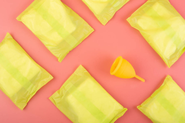 Silicone yellow menstrual cup with pads. Women's health and alternative hygiene on a pink background flat lay. eco-friendly, Alternative reusable product for female hygiene. Minimalism. - 写真・画像