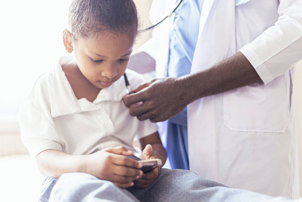 African male pediatrician holding a stethoscope, child, patient, goes to the doctor with mother, black pediatrician checks the lungs, the heart of the child, does the child's examination in the children's hospital, medical care concept. - Foto, afbeelding