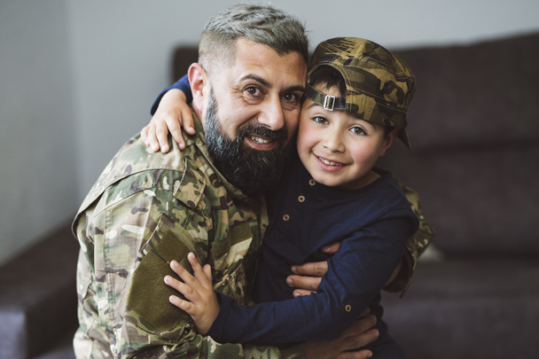 padre militar con su hijo abrazándose mirando a la cámara - niño con gorra militar - concepto de guerra - - Foto, Imagen