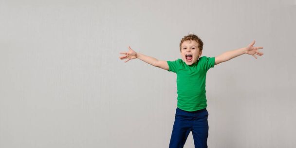 Happy little kid boy in green t-shirt on gray background is smiling, laughing and shaking hands. Children will save the planet concept. Free space for you text and logo - Photo, Image