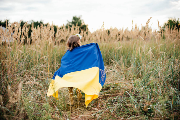 Ukrainian child girl in embroidered shirt vyshyvanka with yellow and blue flag of Ukraine in field. - Foto, Bild