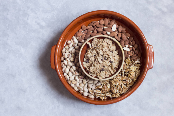 An old earthenware pot filled with mixed dried fruits with a clay bowl filled with toasted rice, whole wheat, and barley flakes with chocolate shavings on a stone textured background.Nuts and cereals.	 - Photo, Image