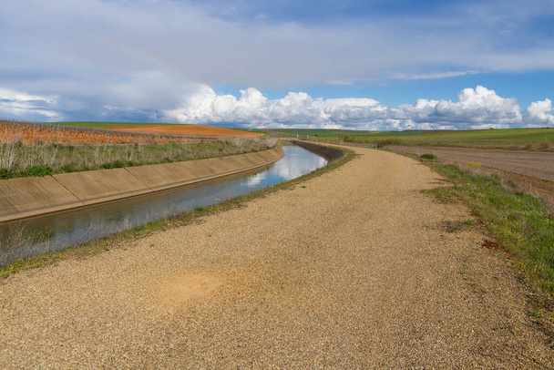 Canal de agua para riego y curva de paisaje agrícola con camino de asfalto paralelo  - Foto, imagen