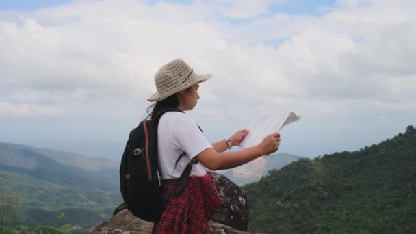 Hipster vrouw met rugzak op zoek naar een kaart op de achtergrond van de bergen. Vrouwelijke wandelaar rustend in de natuur en een kaart lezend. - Video