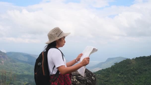 Sırt çantalı hippi kadın dağların arkasındaki haritaya bakıyor. Kadın yürüyüşçü doğada dinleniyor ve bir harita okuyor.. - Video, Çekim