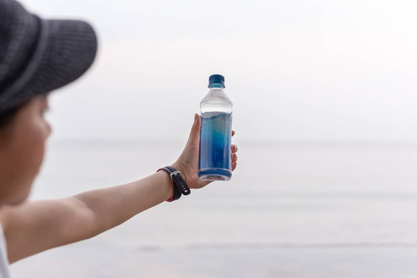 Žena drží láhev minerální vody v ruce na pláži. - Fotografie, Obrázek