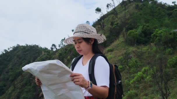 Mulher Hipster com mochila olhando para um mapa no fundo das montanhas. Caminhante feminina descansando na natureza e lendo um mapa. - Filmagem, Vídeo