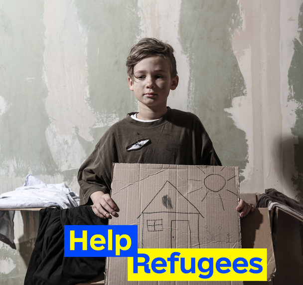 段ボールの上に家の写真を持つホームレスの小さな男の子。ウクライナ難民を助ける - 写真・画像