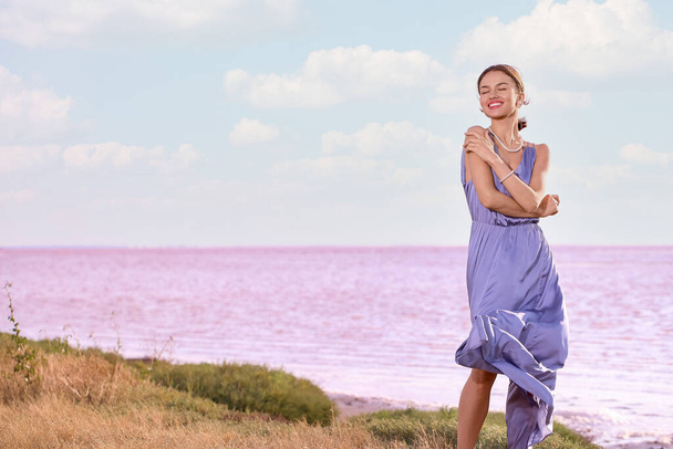 Mujer joven con estilo posando cerca del lago rosa en el día de verano - Foto, imagen