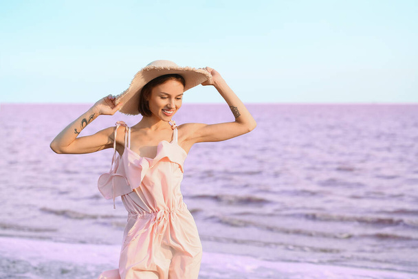 Stijlvolle jonge vrouw poseren in de buurt van roze meer op zomerdag - Foto, afbeelding