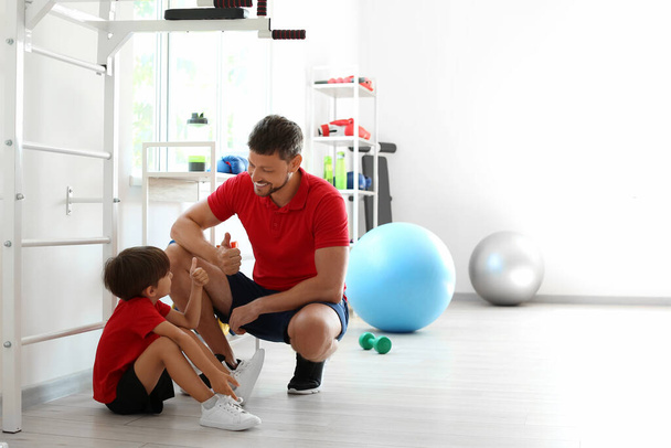Entrenador masculino y niño pequeño mostrando pulgar hacia arriba en el gimnasio - Foto, imagen