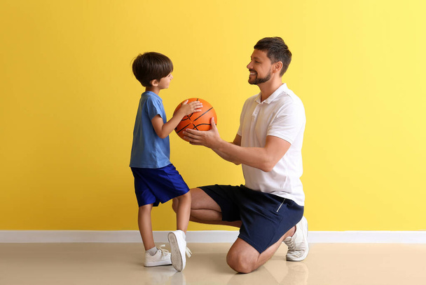 男性コーチとともにボールと彼の小さな訓練生近く黄色の壁 - 写真・画像