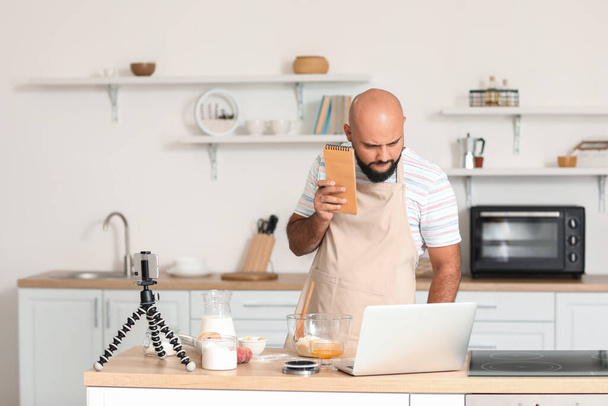 Hezký muž s notebookem sledování vaření video tutorial na notebooku v kuchyni - Fotografie, Obrázek