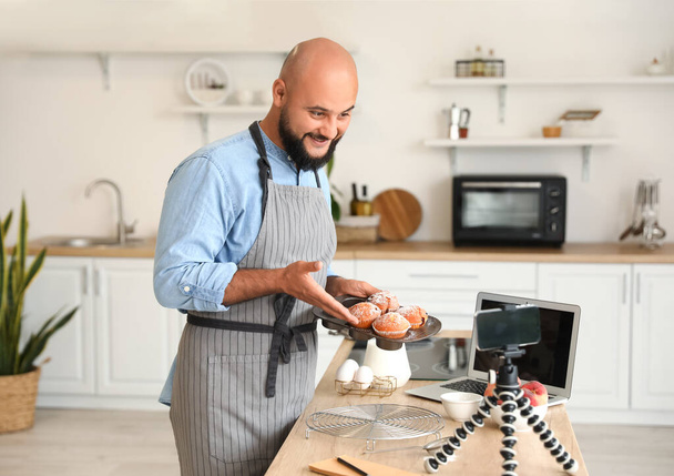 Hombre guapo con sabrosas magdalenas de melocotón grabación de vídeo en la cocina - Foto, imagen