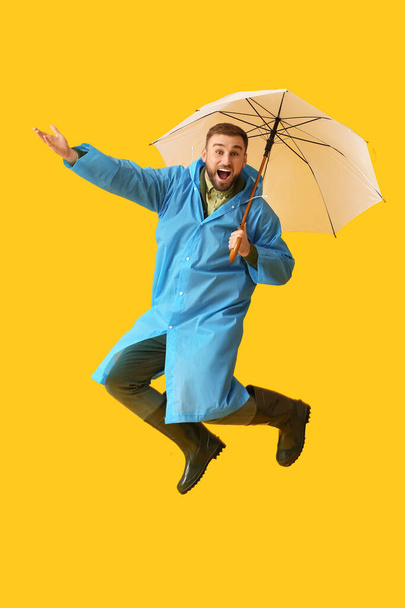 Skoky mladý muž ve stylovém plášti a s deštníkem na barevném pozadí - Fotografie, Obrázek