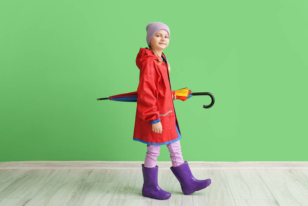 Little girl in stylish raincoat and with umbrella near color wall - Foto, afbeelding