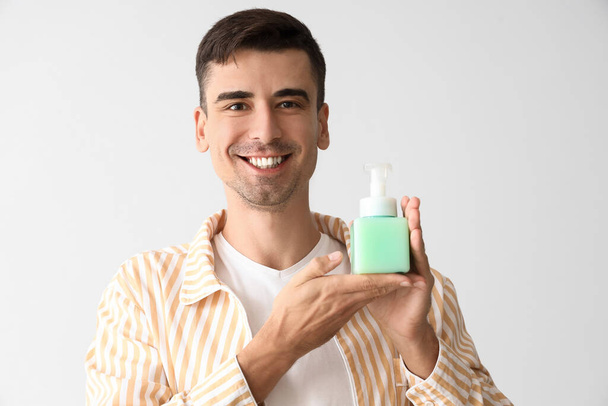 Handsome young man with liquid soap on light background - Foto, Imagem