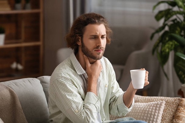 Ill man with sore throat drinking hot tea at home - Fotografie, Obrázek