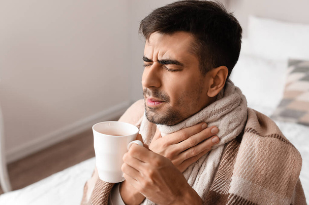 Joven enfermo con dolor de garganta bebiendo té caliente en casa - Foto, imagen