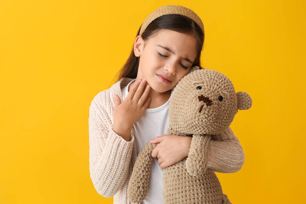 triest klein meisje met speelgoed lijden aan zere keel op gele achtergrond - Foto, afbeelding