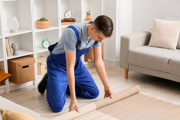 Male worker rolling stylish carpet in room - Foto, Imagen