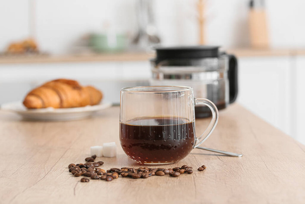 Стеклянная чашка кофе и бобов на деревянном прилавке на кухне, крупный план - Фото, изображение
