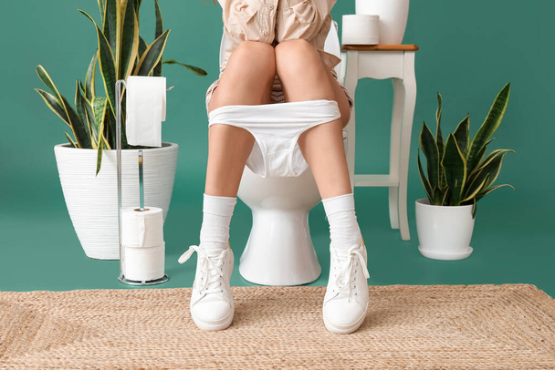 Mladá žena sedí na záchodové míse na zeleném pozadí - Fotografie, Obrázek