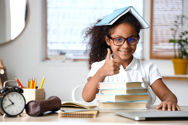 Маленька афро-американська дівчина з книгами, які показують пальцем вгору вдома. - Фото, зображення