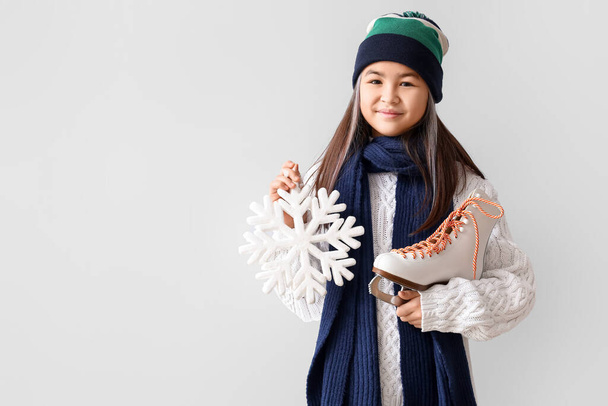 Little Asian girl in warm clothes with ice skate and snowflake on light background - Photo, Image