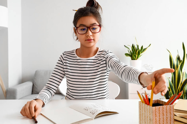 Pequeña chica asiática tomando lápiz mientras estudia con tutor en línea en casa - Foto, Imagen