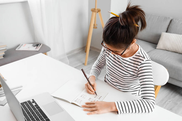 Menina asiática escrevendo em copybook durante a aula on-line em casa - Foto, Imagem