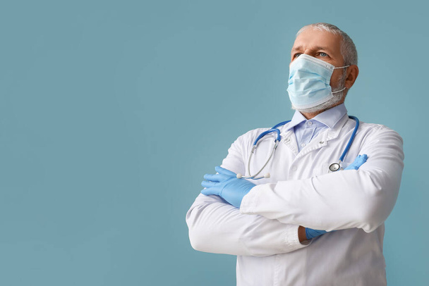 Mature médecin masculin en masque médical avec stéthoscope sur fond bleu - Photo, image