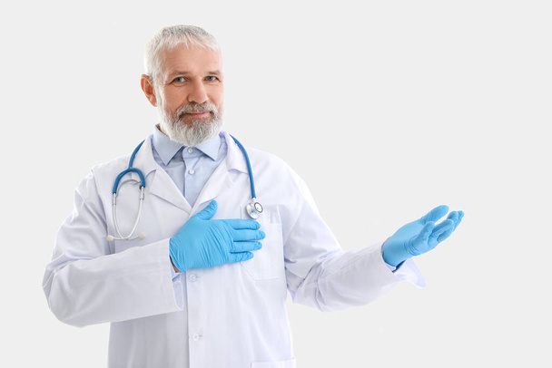 Mature médecin masculin avec stéthoscope montrant quelque chose sur fond blanc - Photo, image