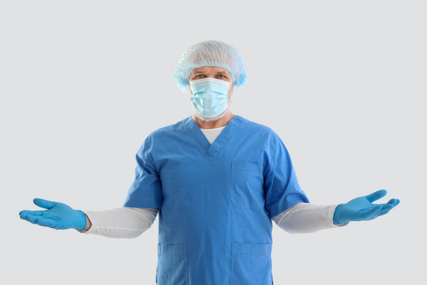 Volwassen mannelijke arts in medisch masker en handschoenen op witte achtergrond - Foto, afbeelding