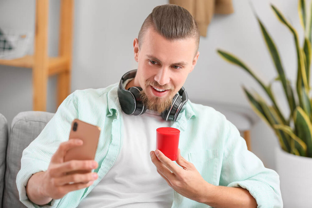 Man holding wireless portable speaker and mobile phone on sofa - Foto, immagini