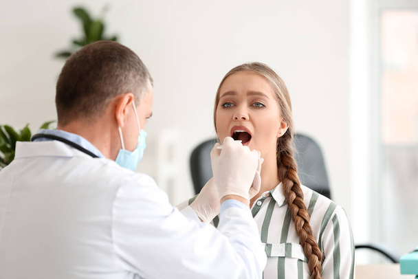 Doctor examining woman with sore throat in clinic - Fotoğraf, Görsel