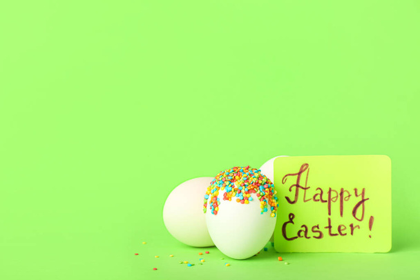 Eggs with sprinkles and text HAPPY EASTER on green background - Fotografie, Obrázek