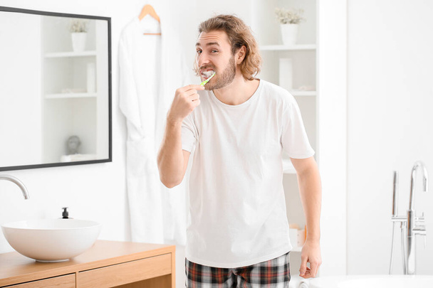 Knappe jongeman tandenpoetsen in de badkamer - Foto, afbeelding