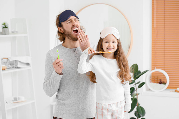 Μικρό κορίτσι και ο πατέρας της με μάσκες ύπνου βουρτσίζουν τα δόντια στο μπάνιο - Φωτογραφία, εικόνα