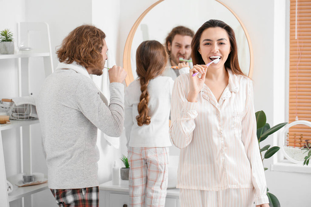 Young woman with her husband and little daughter brushing teeth in bathroom - Foto, Bild