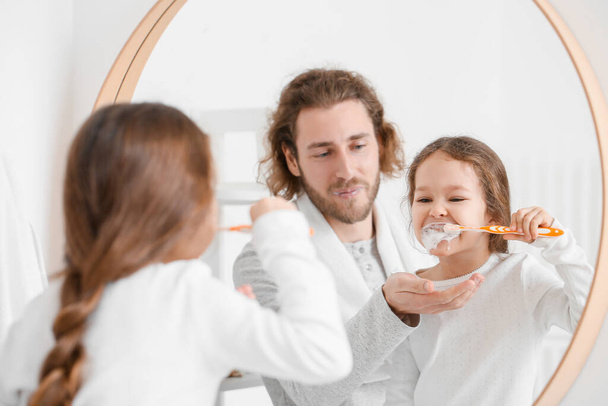 Little girl with her father brushing teeth near mirror in bathroom - Fotoğraf, Görsel